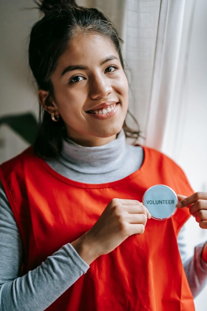 Confident female volunteer smiling while holding a volunteer badge indoors.