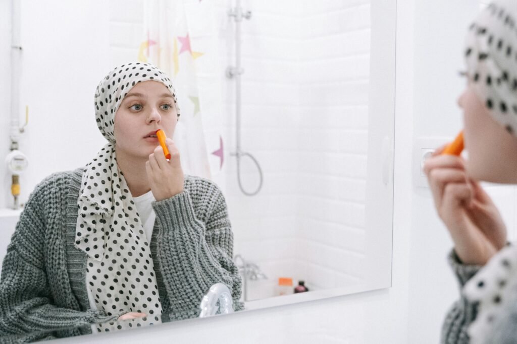 A woman in a headscarf applies lip balm, symbolizing strength and cancer awareness.